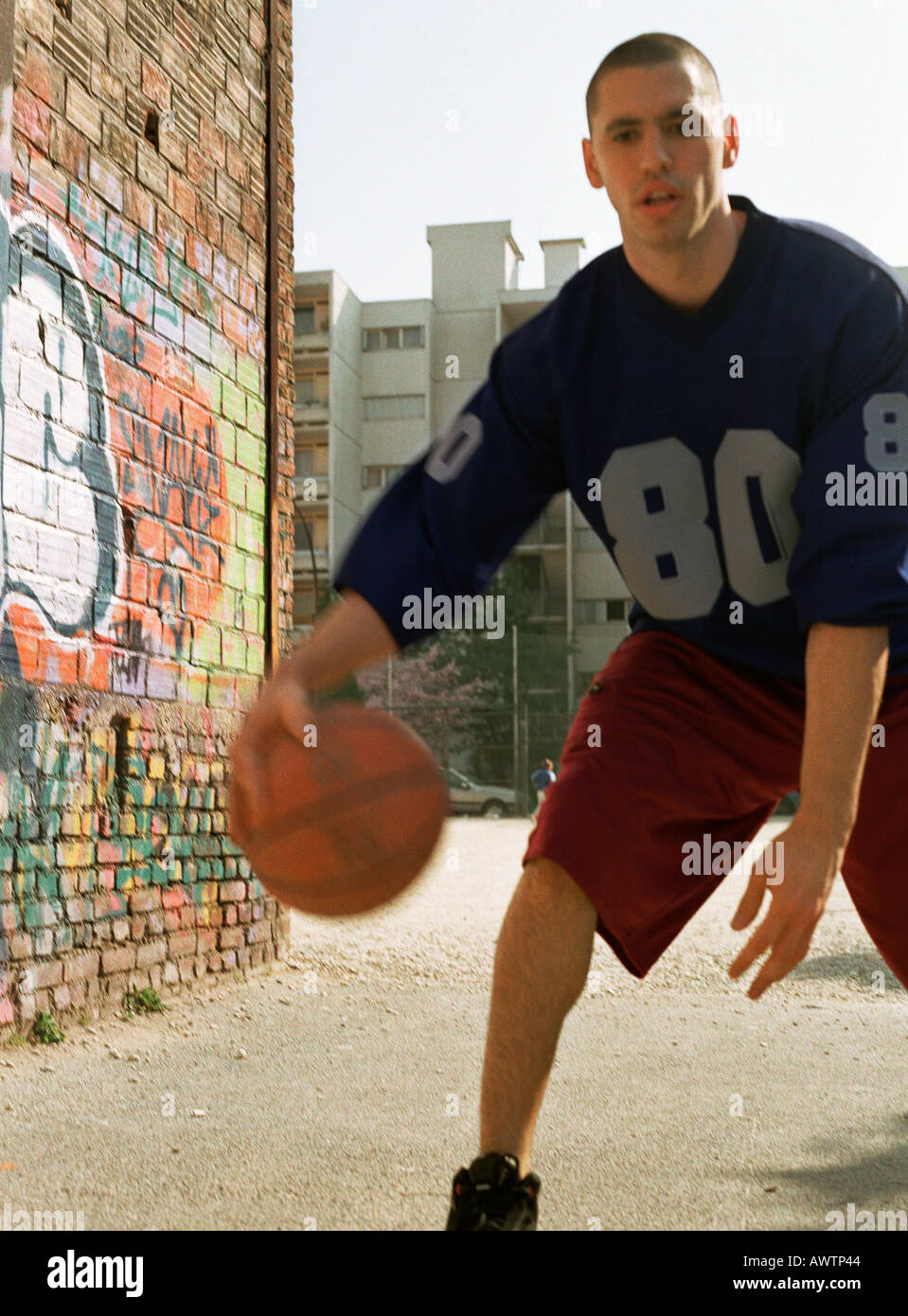 Mann dribbling Basketball in städtischen Spielplatz neben Graffitied Wand Stockfoto