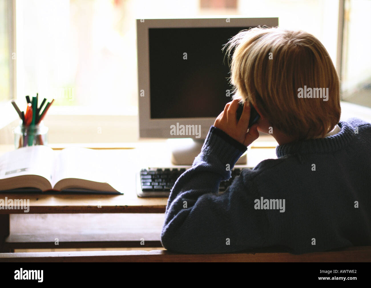 Kleiner Junge sitzt am Computer, telefonieren, Rückansicht Stockfoto