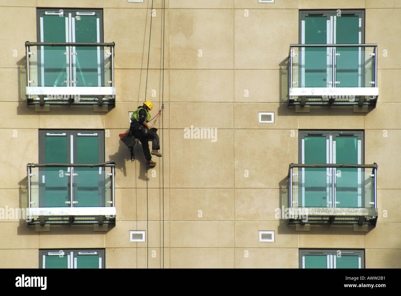 Arbeiter im Stuhl Gurt unterstützt vom Dach montiert Kabel Durchführung von Reinigungsarbeiten auf neue Wohnblocks Wand Stockfoto