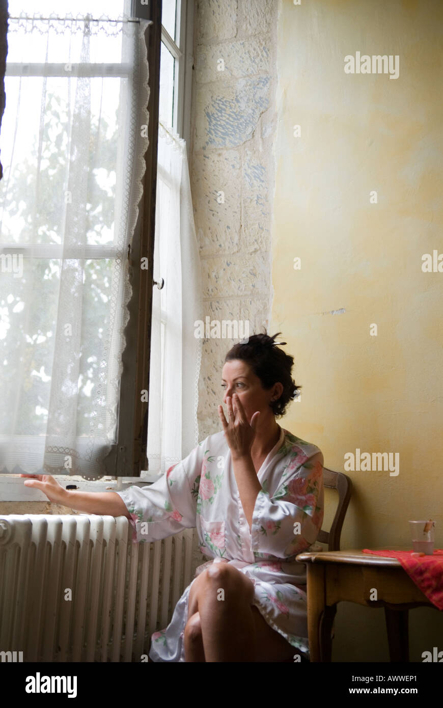 Frau in ihrer Mitte der vierziger Jahre durch die großen Fenster im Hotel in Arles, Provence, Frankreich sitzt und schläfrig wischt ihr Auge Stockfoto