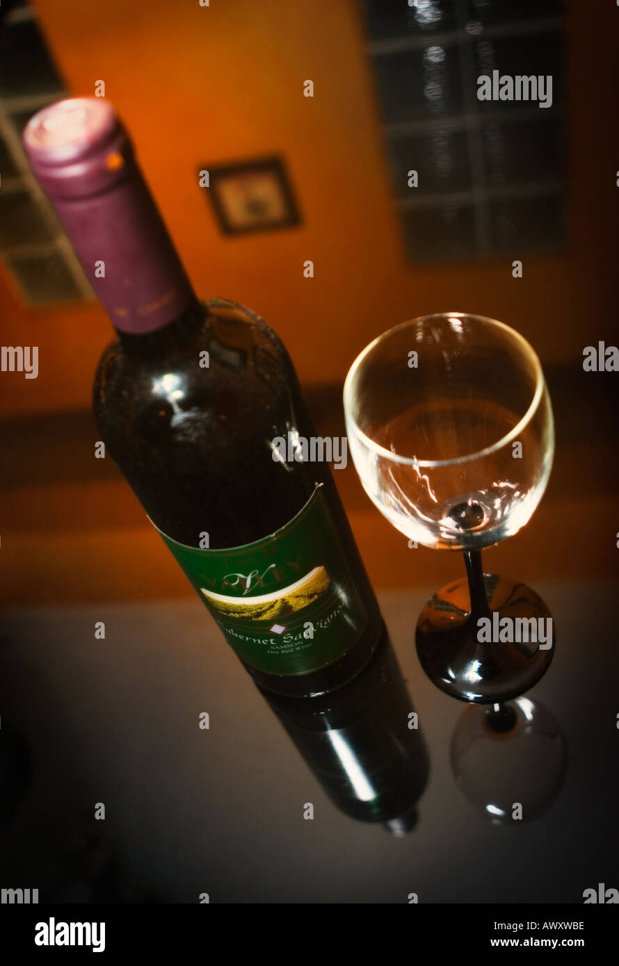 Ungeöffnete Flasche Wein und leeres Glas auf einem Tisch in einem abgedunkelten eleganten Speisesaal Stockfoto