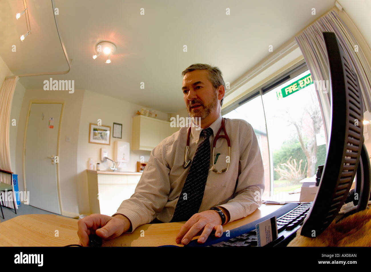 Männliche englische weiße Allgemeinmedizin GP Hausarzt Rücksprache mit Stethoskop und Computer im Arbeitszimmer England GB UK Stockfoto