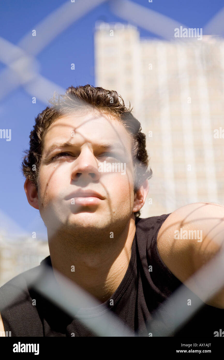 Ein junger Mann hinter einem defokussierten Maschendrahtzaun Stockfoto