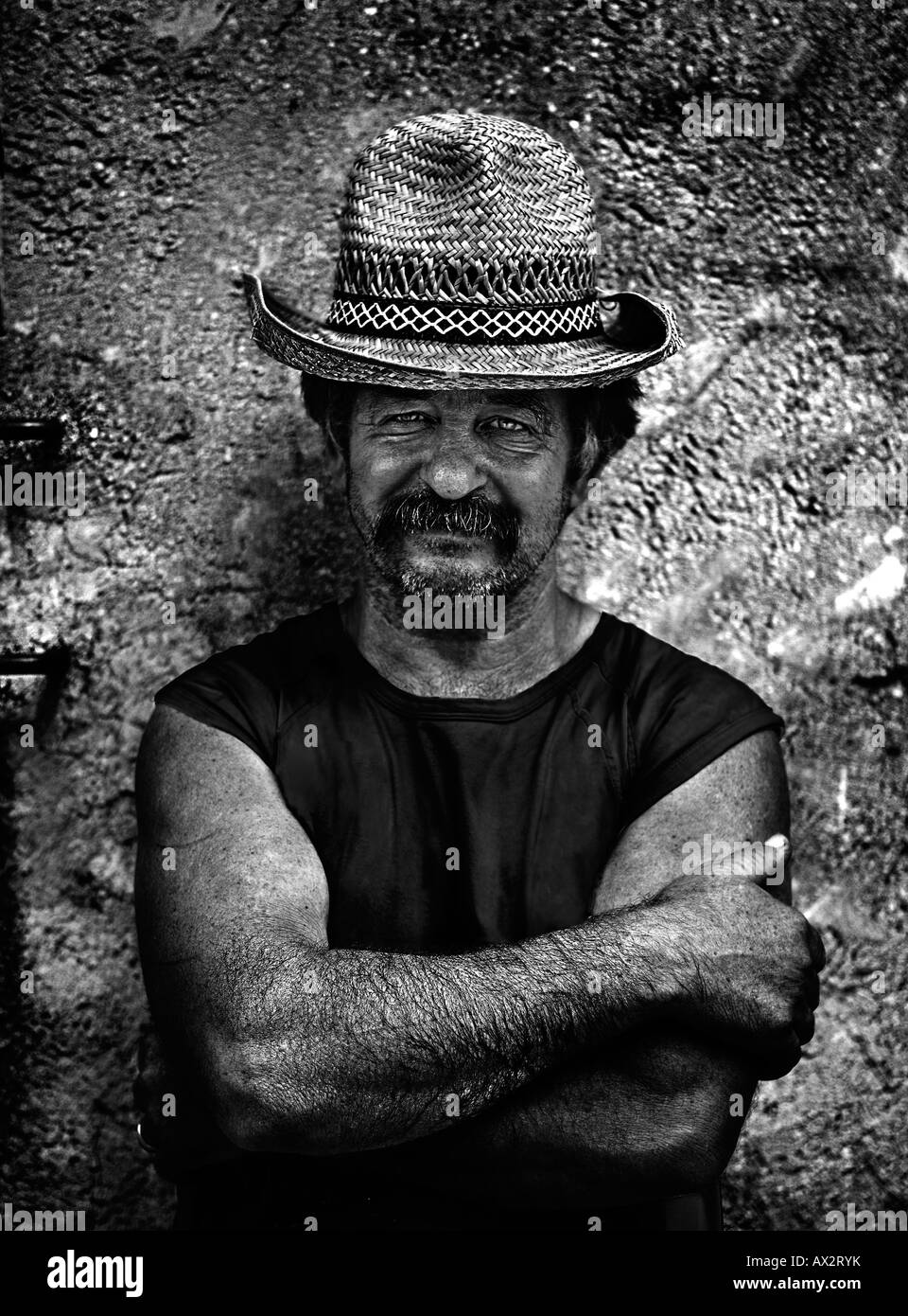 Sizilianische Landwirt steht gegen eine alte Mauer, verschränkten Armen und ein Strohhut schützt ihn vor der Sonne. Stockfoto