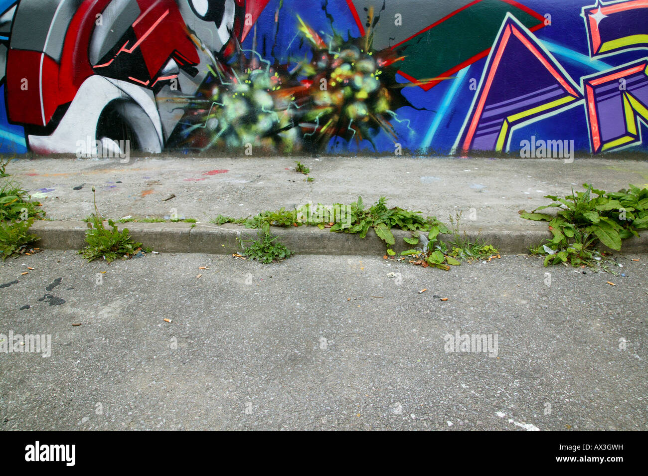 Graffitiwand abgedeckt und überwucherten Fußweg Zigarettenkippen überall verstreut Stockfoto
