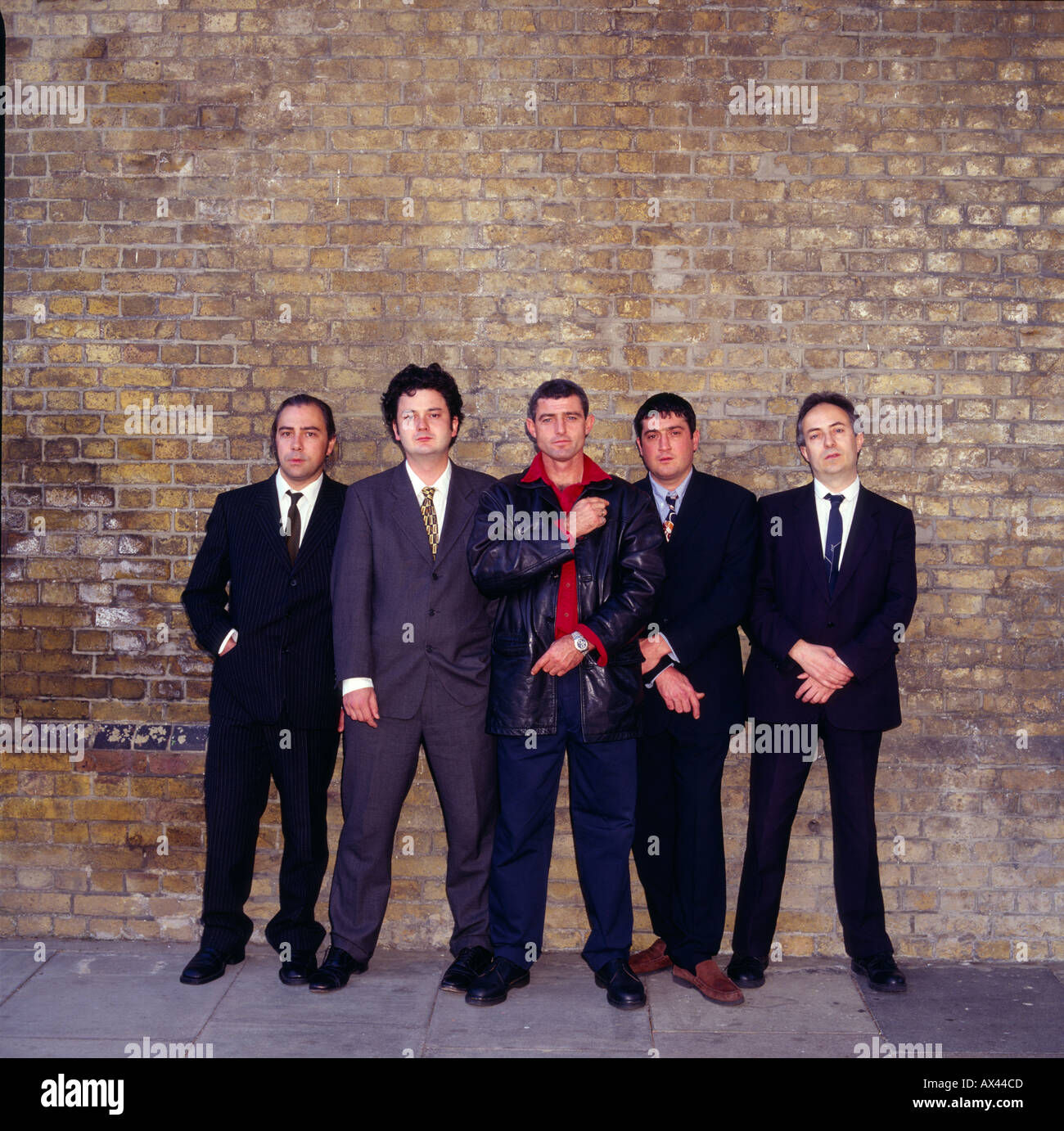 Die üblichen Verdächtigen. Bande von Männern gegen Backsteinmauer. Jahrgang 1990s Stockfoto