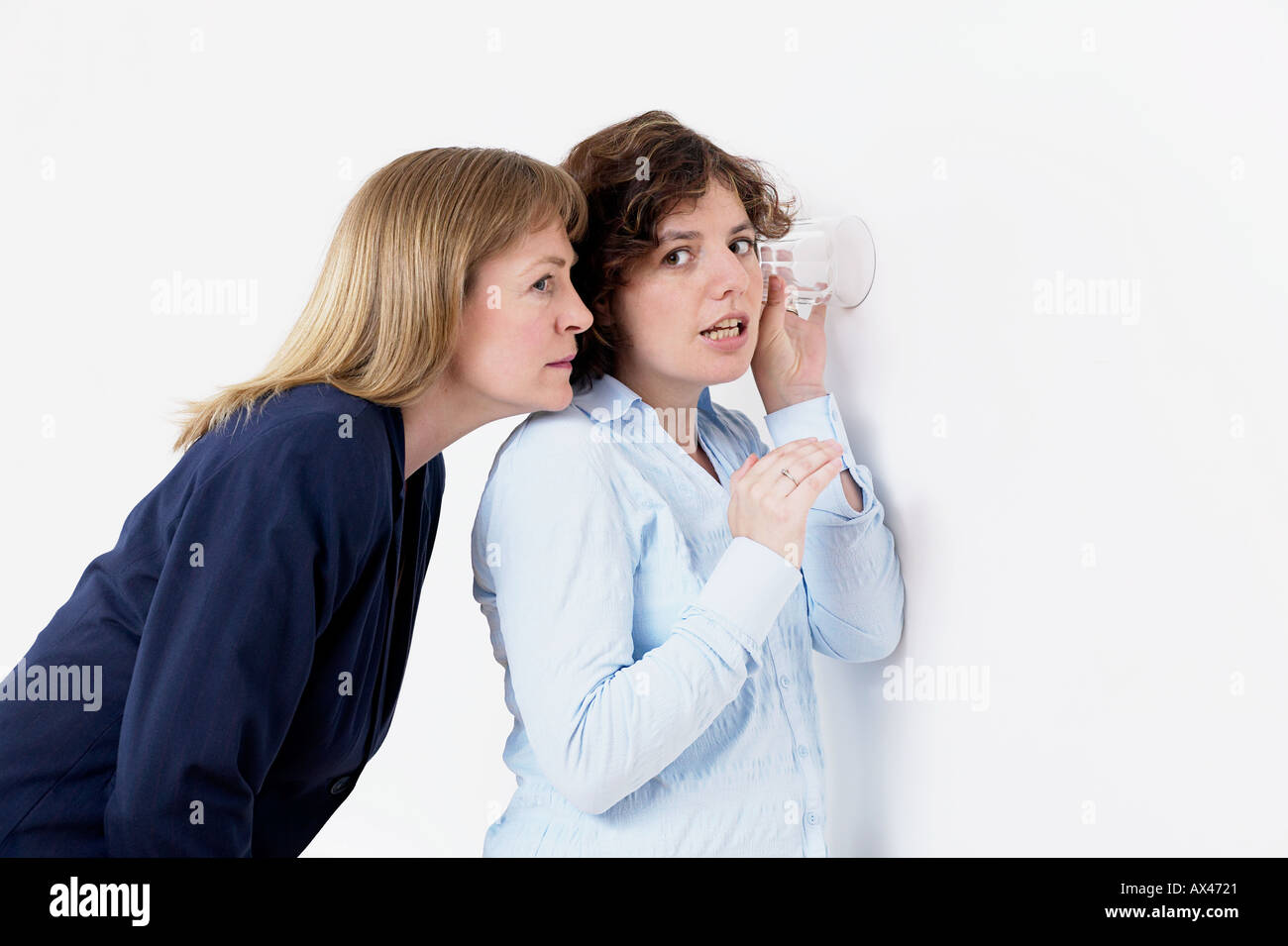 Frau anhören Gespräch durch Wand mit ein offenes Ohr für ein Glas Stockfoto