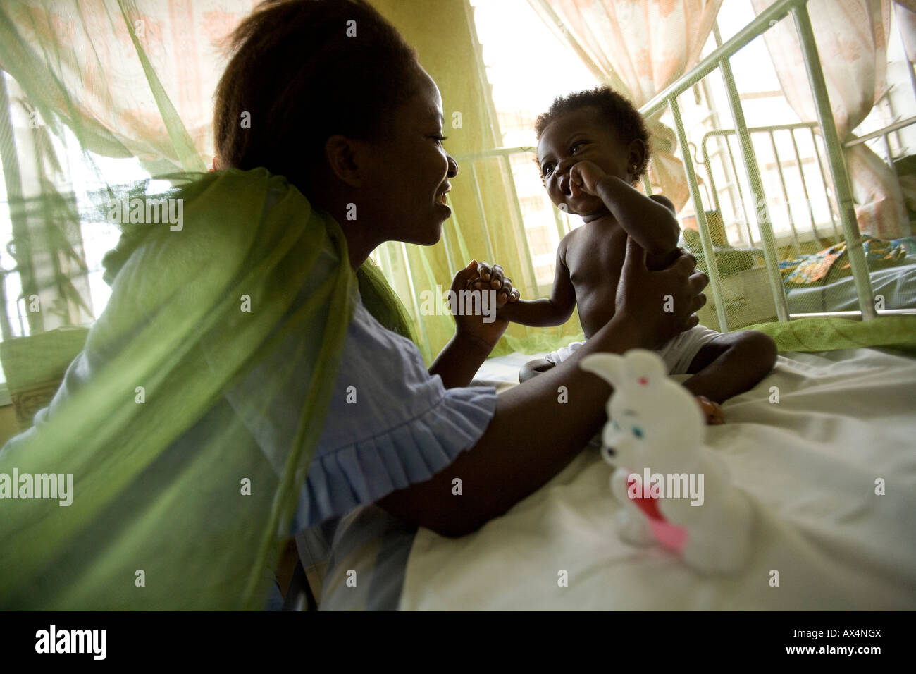 Eine Frau besucht ihr kleines Mädchen, unter einem Moskitonetz sitzt Stockfoto