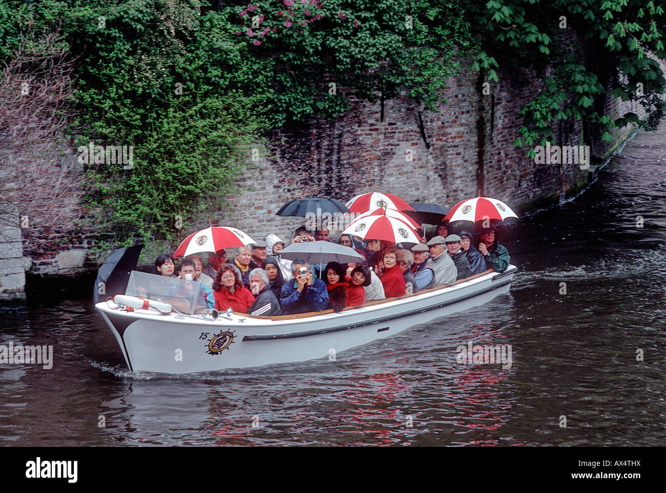 Touren durch die Kanäle von Brügge, Belgien mit Sonnenschirmen im Regen. Stockfoto