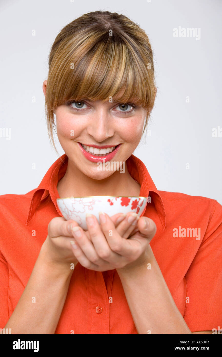 Junge Frau hält Teeschale, Lächeln, Porträt Stockfoto