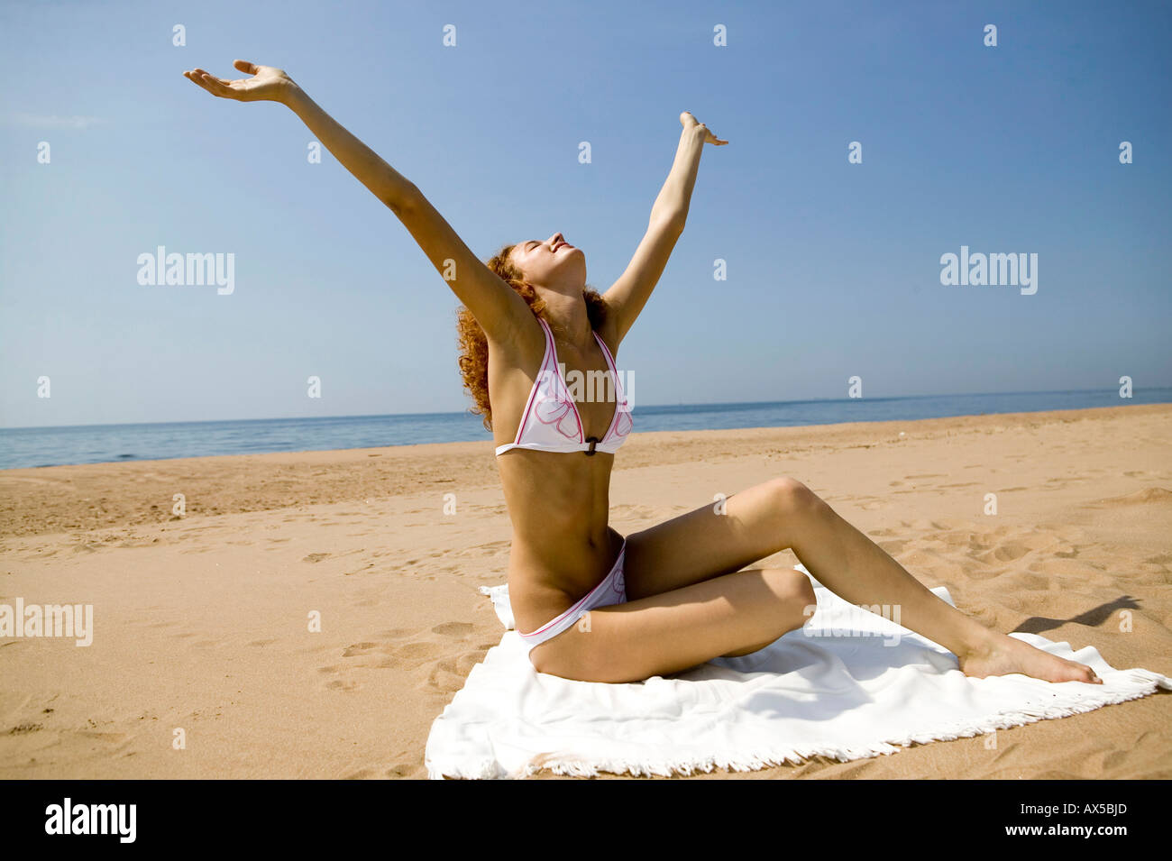 Junge Frau sitzt auf Badetuch, streckte Arme Stockfoto