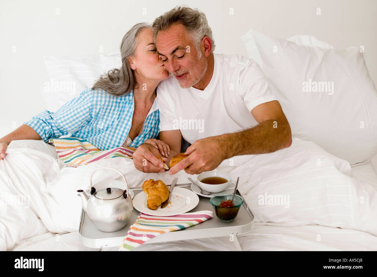 Älteres Paar sitzt am Bett mit Frühstück, Frauen küssen Mann Stockfoto