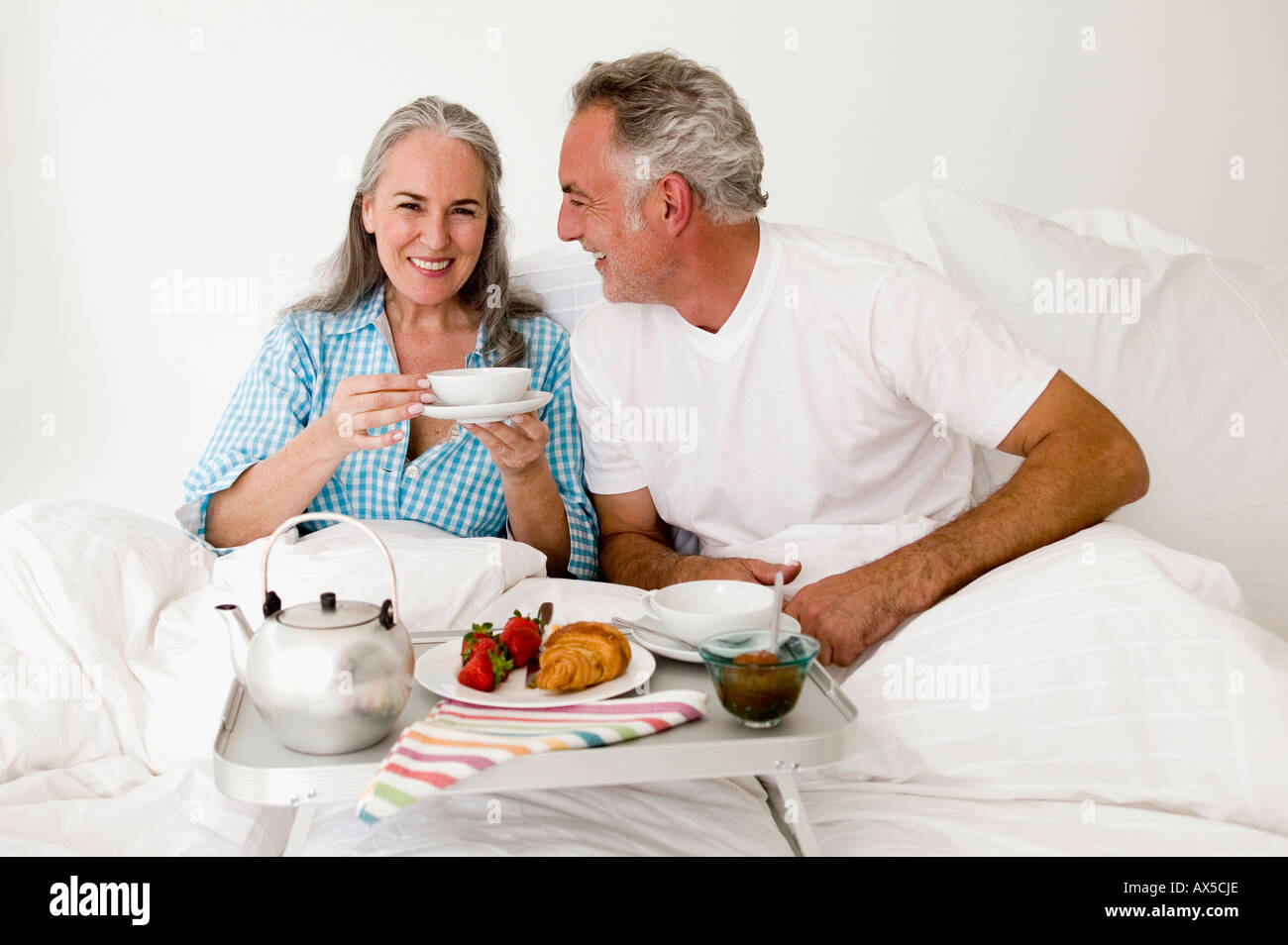 Älteres Paar sitzt auf dem Bett mit Frühstück, Lächeln Stockfoto