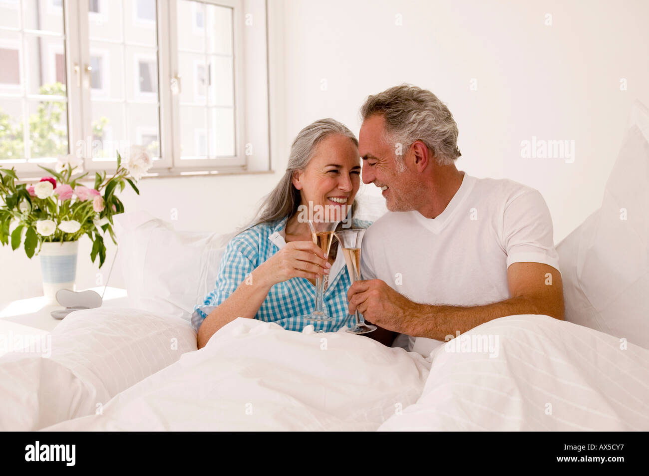 Älteres Paar auf Bett Toasten Champagner, Lächeln Stockfoto