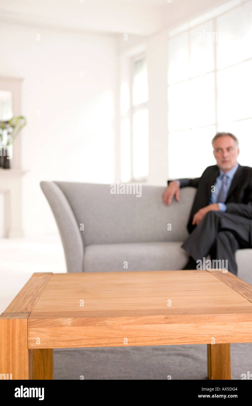 Reifer Mann auf Sofa sitzen, schauen weg (Fokus auf Tisch im Vordergrund) Stockfoto