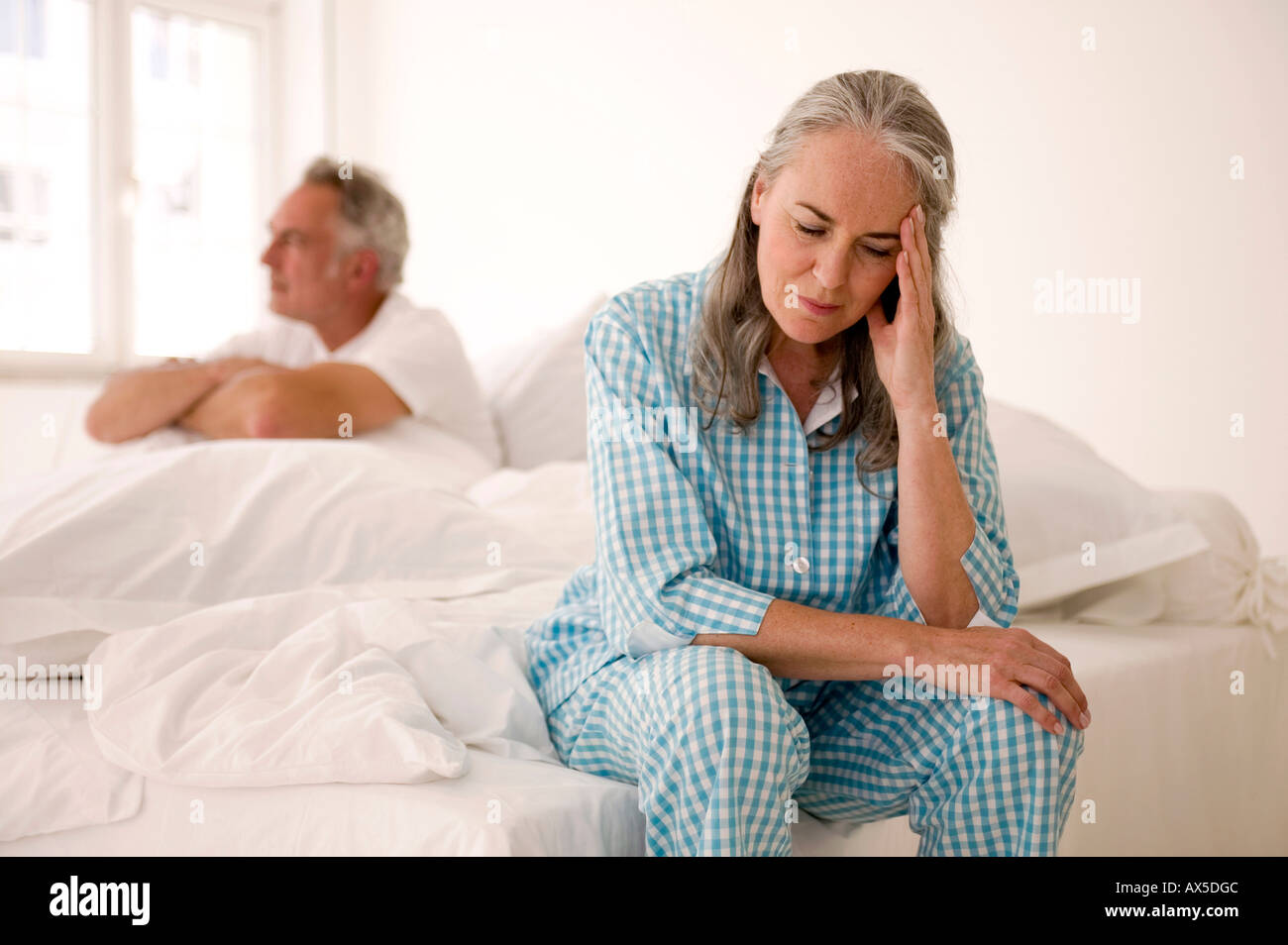 Älteres Paar sitzt auf Bett (Schwerpunkt: Frau im Vordergrund mit Kopf in Händen) Stockfoto