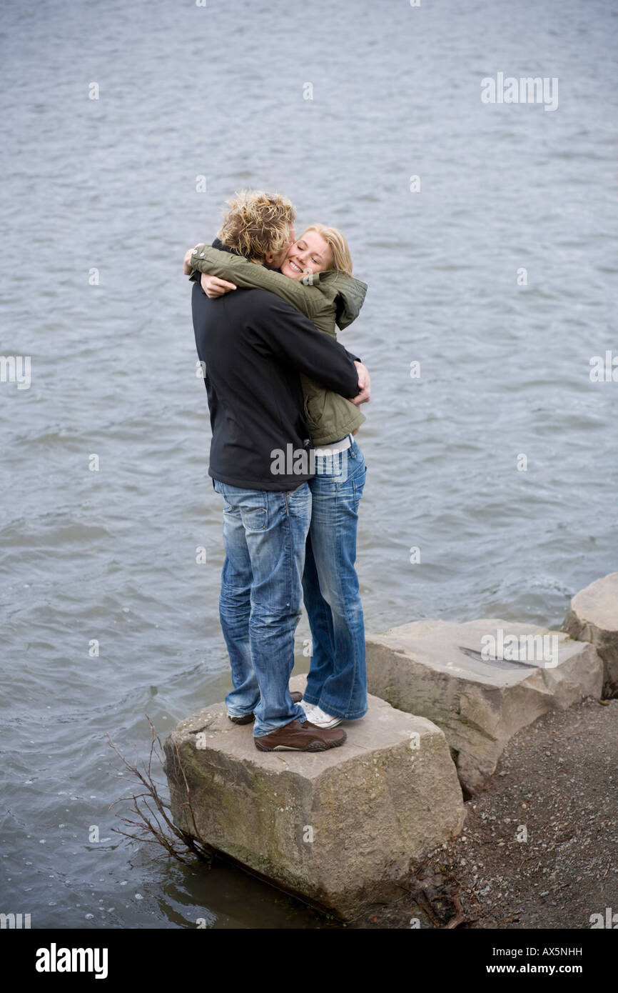 Paar steht auf einem Felsen am Rand des Wassers, umarmen einander Stockfoto