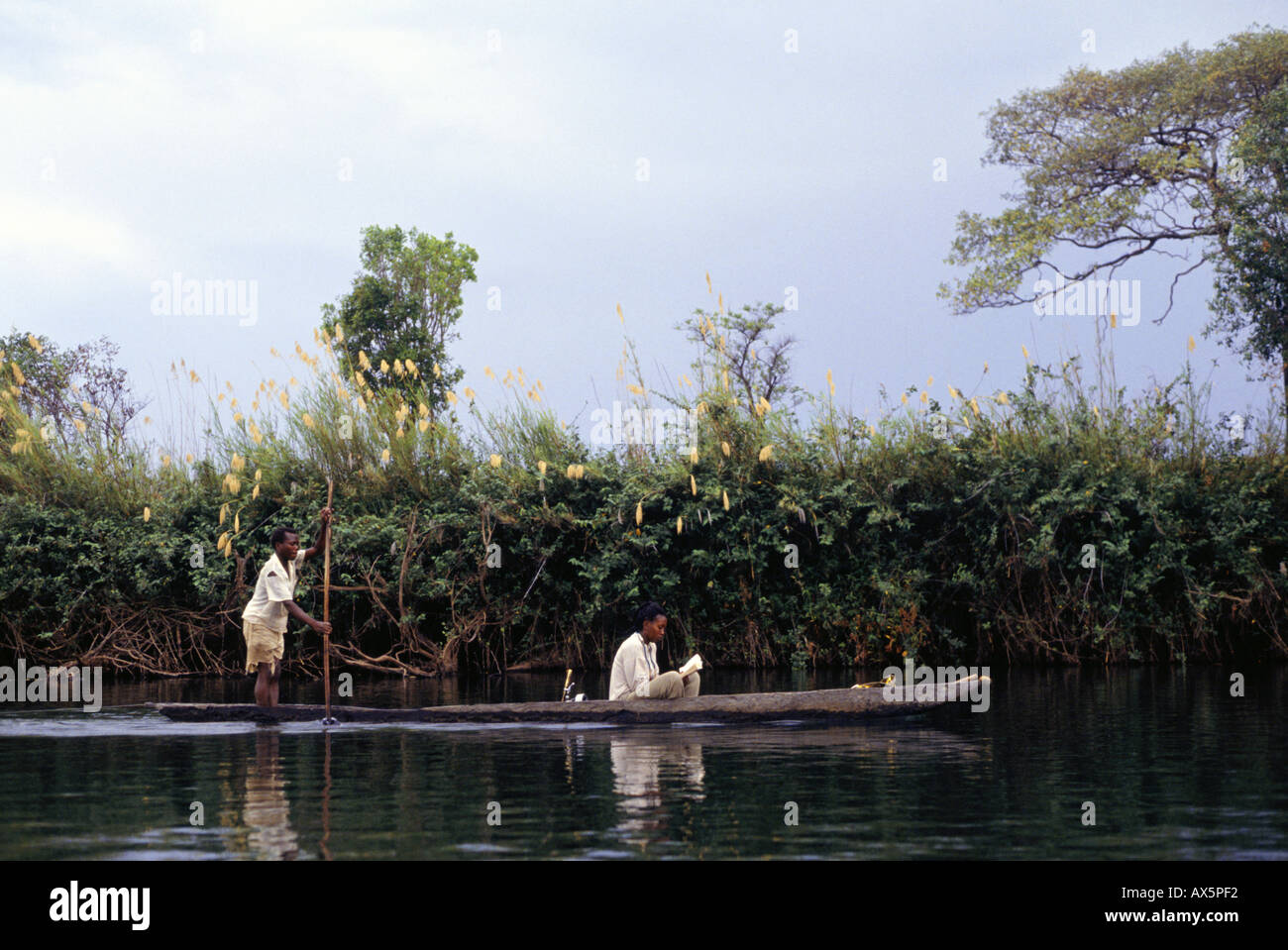 Sambia. Sambische Frau in einem ausgegraben Kanu mit Mann polling das Kanu zu lesen. Stockfoto
