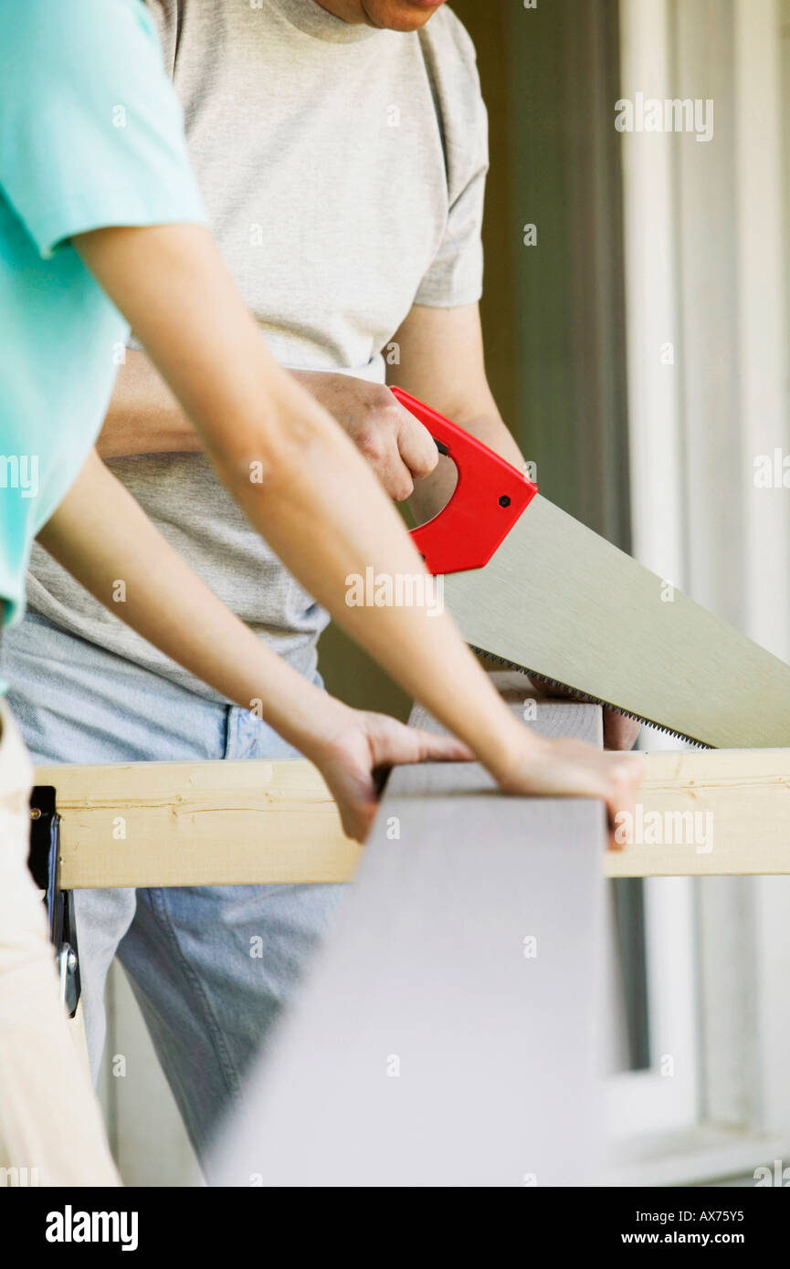 Nahaufnahme von einer Frau mit einem Mann eine Brett mit einer Säge zu schneiden Stockfoto