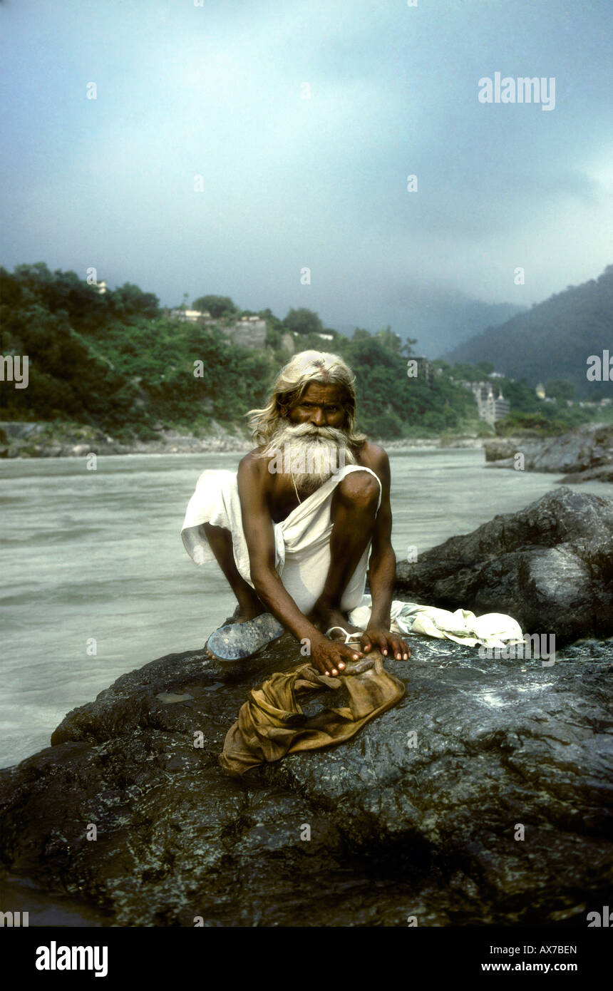 Ein religiöser Mann hockt auf ein kühner von der Seite des Gangees, seine Wäsche waschen, die er uns, hinter dem Himalaya starrt Stockfoto