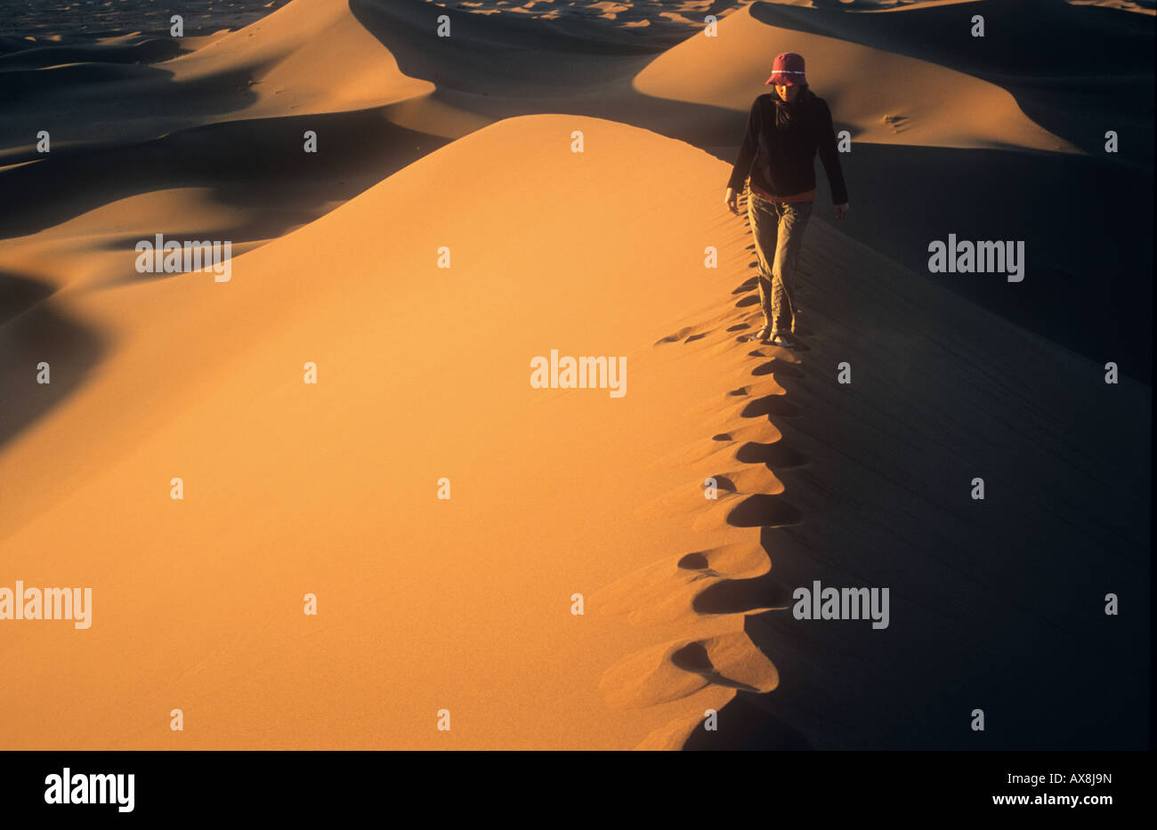 Frau zu Fuß auf dem Kamm einer Düne kurz nach Sonnenaufgang, Erg Chigaga, Sahara, Marokko. Stockfoto