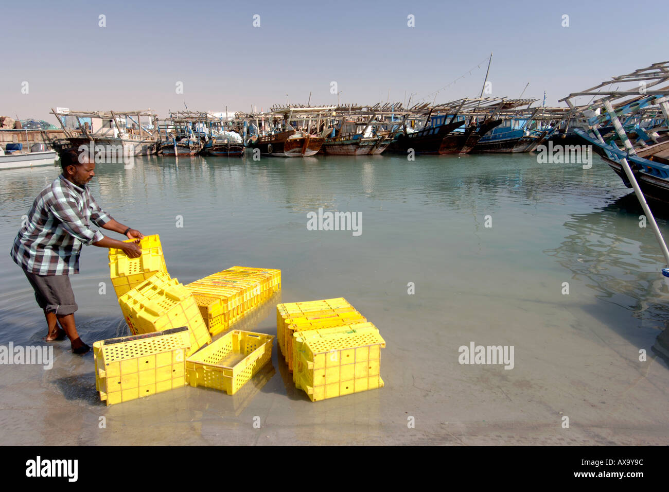 Ein Fischer waschen gelbe Kisten im Hafen des Fischerdorfes Al Khor in Katar. Stockfoto