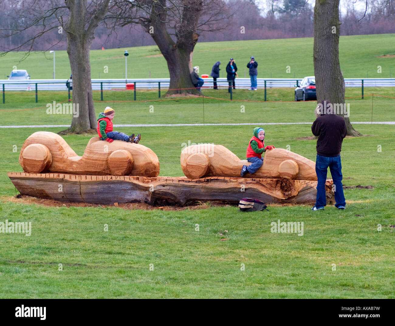 Kleine Kinder spielen auf hölzernen Racing Car Skulptur aus umgestürzten Baum am Oulton Park Motor Race Track Cheshire England geschnitzt Stockfoto