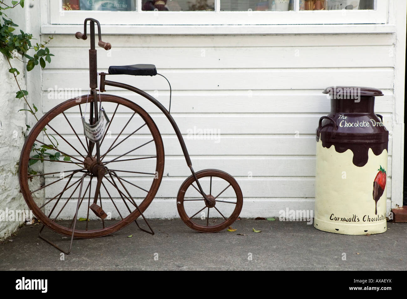 Ein Hochrad Fahrrad und Milchkanne vor einem Geschäft in Polperro, Cornwall Stockfoto
