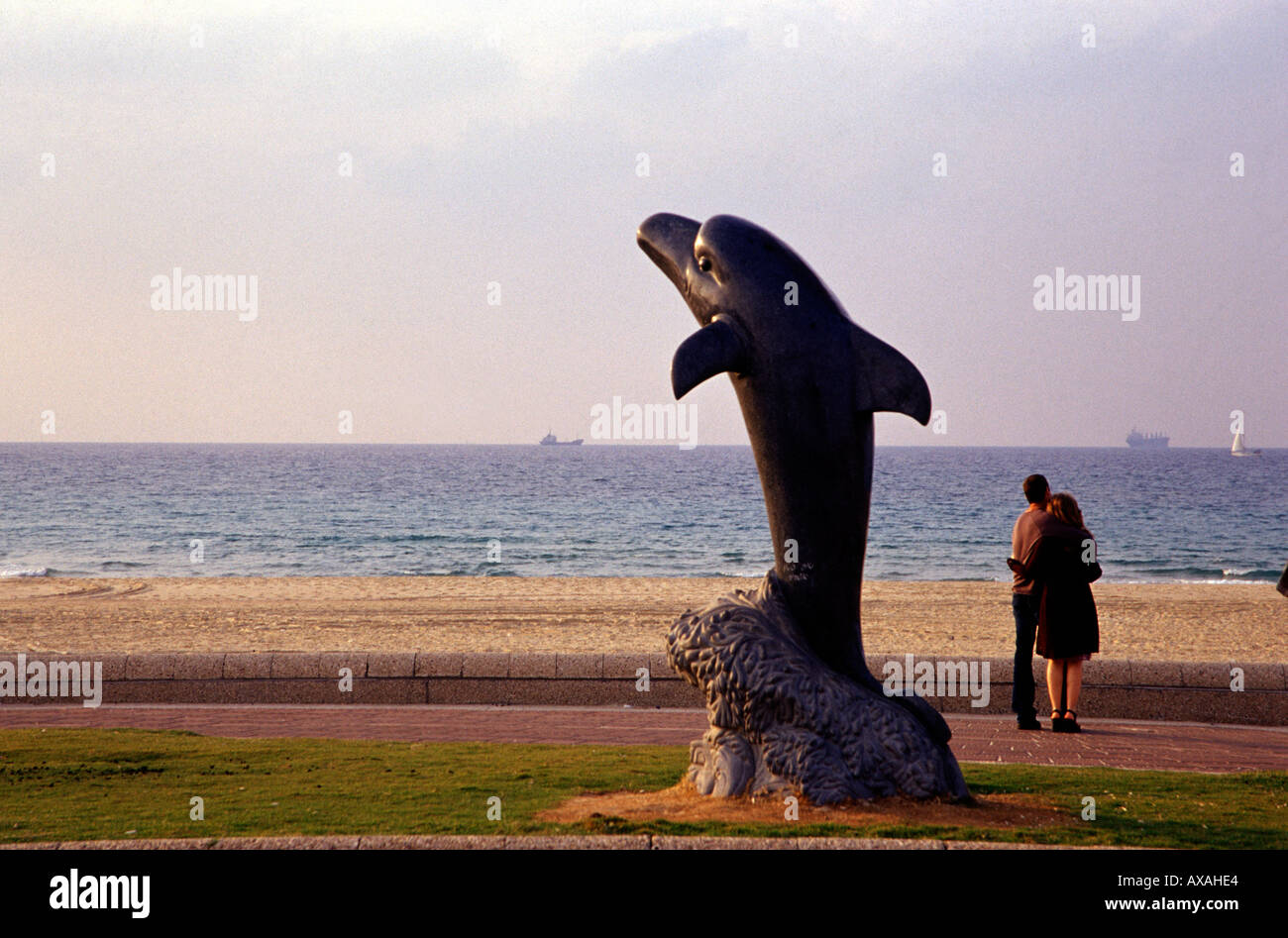 Ein paar Umarmungen neben einer zeitgenössischen Skulptur mit der Darstellung eines Dolphin an der Küste Promenade der Stadt Ashdod in Israel. Stockfoto