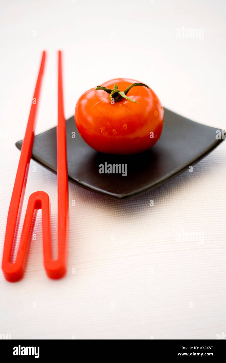 Eine rote Tomaten und roten Stäbchen auf einem quadratischen schwarzen orientalische Teller Stockfoto