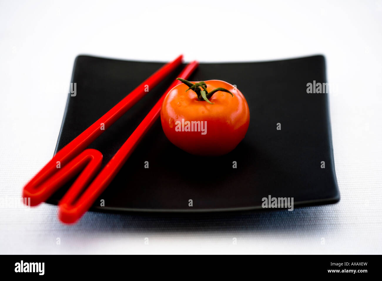 Eine rote Tomaten und roten Stäbchen auf einem quadratischen schwarzen orientalische Teller Stockfoto
