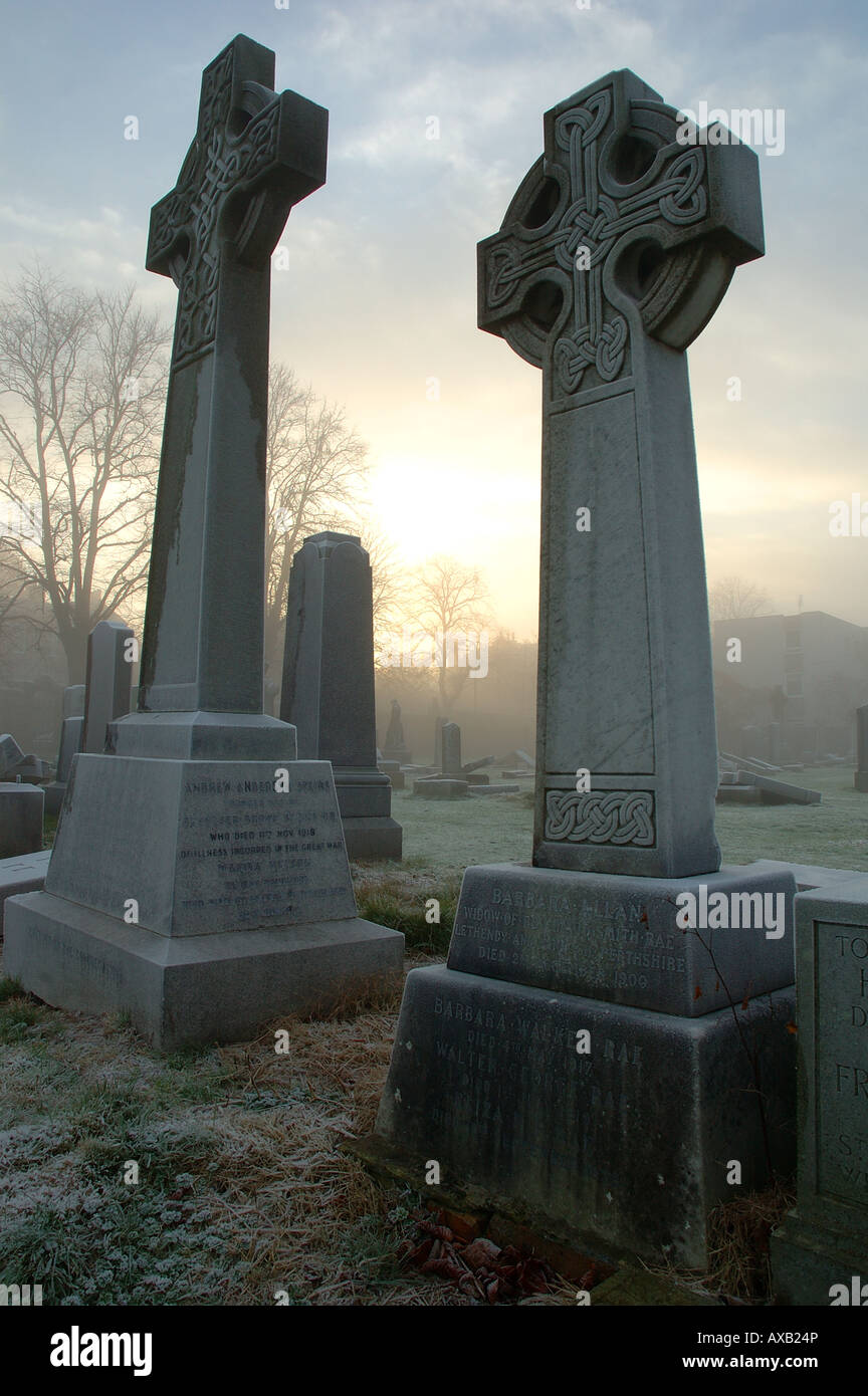 Keltisches Kreuz Grabsteine auf einem Friedhof an einem frostigen Nebel Morgen mit einem tief stehender Sonne gefüllt Stockfoto
