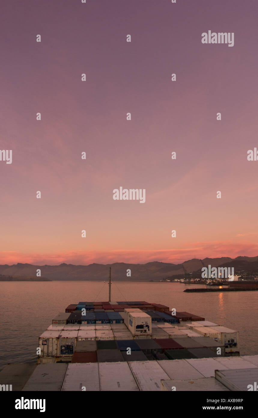 Ein Containerschiff nähert Hafen sich während einem rosa Sonnenaufgang Stockfoto