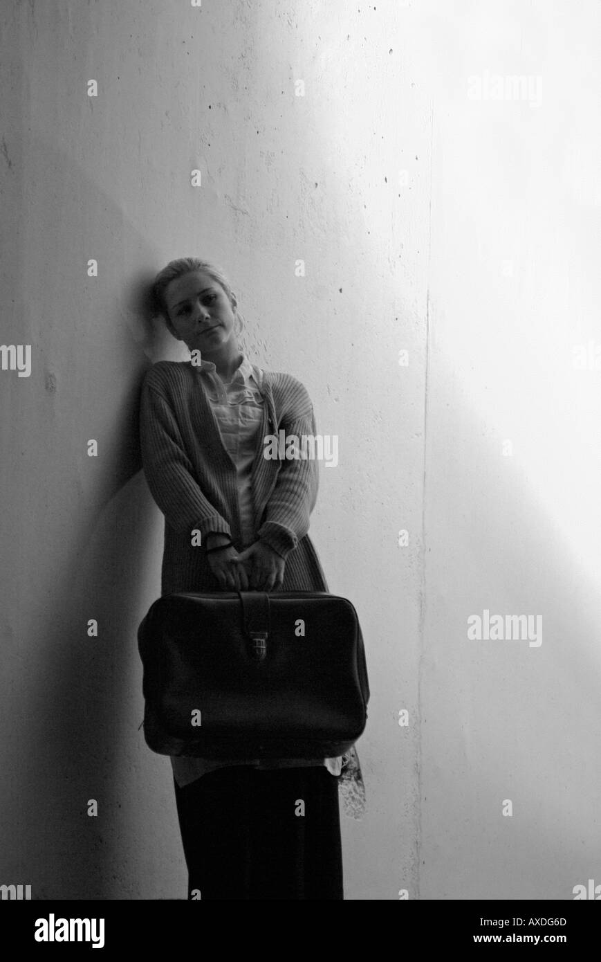 Einsame Frau mit einem Koffer an einer Wand unter Straßenbeleuchtung Stockfoto