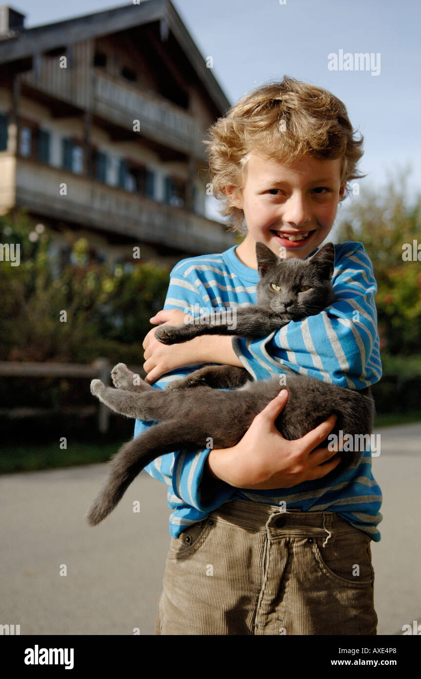 Neun Jahre alten Jungen Holding Katze vor bayerischen Bauernhaus Stockfoto
