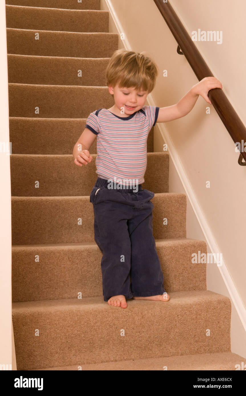 Junge Kleinkinder, 2 Jahre alt, geht vorsichtig die Treppe hinunter und hält sich am Geländer fest Stockfoto