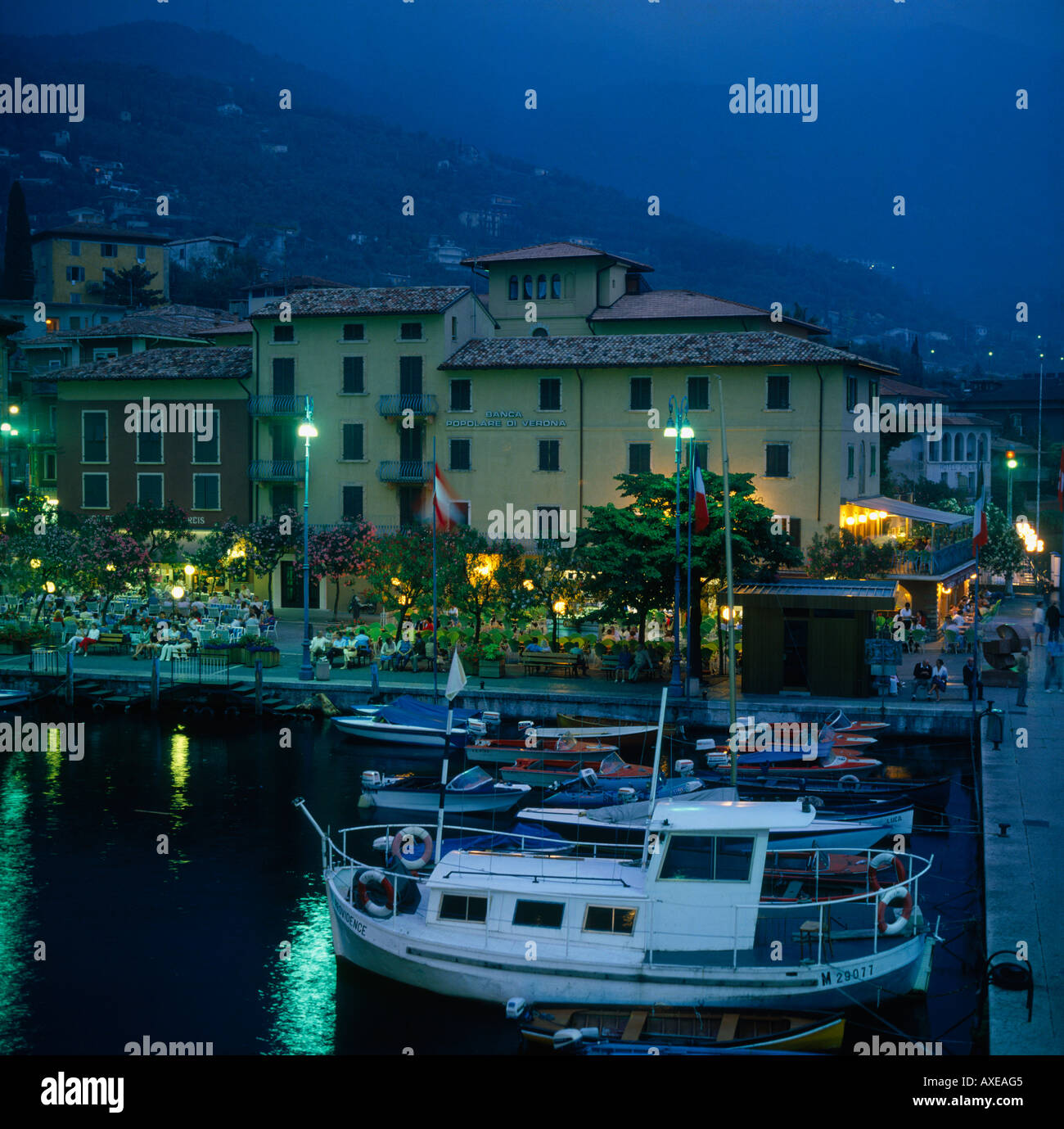 Uferpromenade von Malcesine Hafen in der Abenddämmerung mit Restaurants Boote mit Hügeln im Hintergrund auf See Garda Lombardei Provinz Italien Stockfoto
