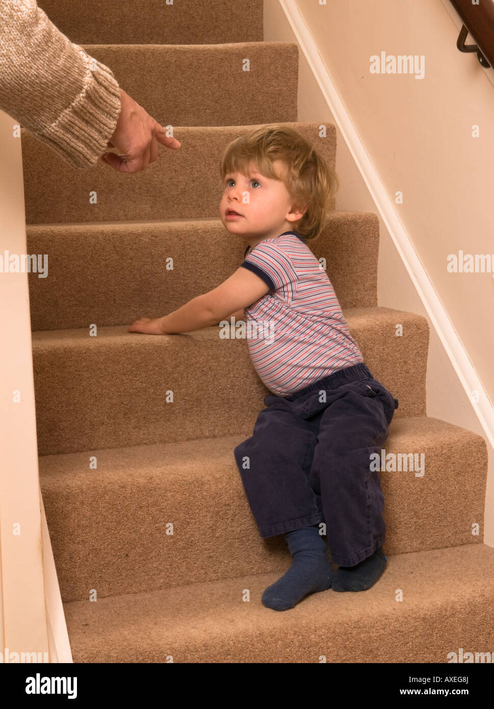 Der zweijährige Junge soll unten auf der Treppe sitzen, vielleicht als Teil der Disziplin auf einem "frechen Schritt", oder einfach nur, um ruhig zu sein und mit der Hand zu zeigen Stockfoto