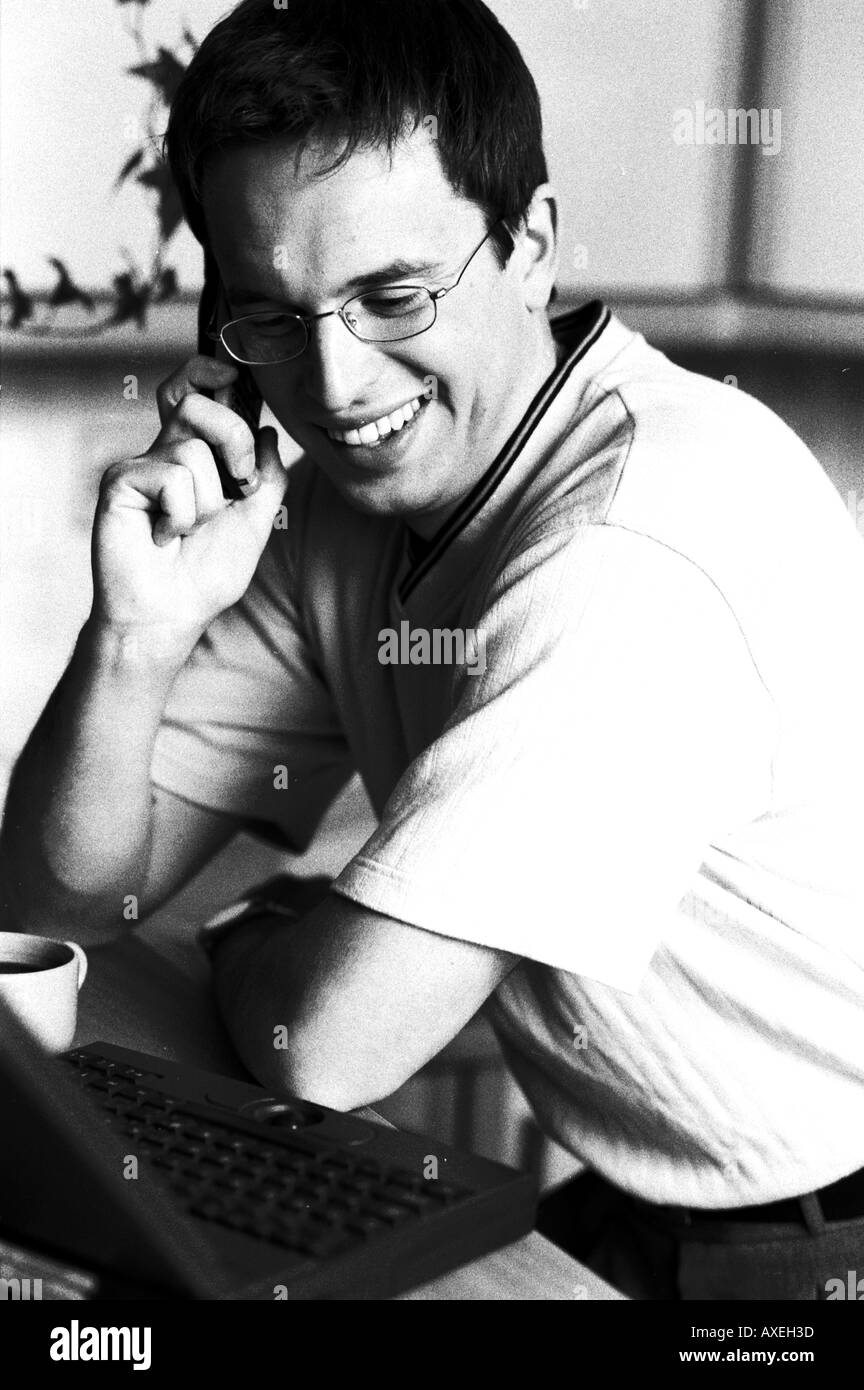 Mann männlich Alter 30 35 dunklen Haaren reden Sit lächeln lächelnd glücklich fröhliche Lachen Arbeit Brille Computer Laptop Ohr Handy Kopfhörer Informat Stockfoto