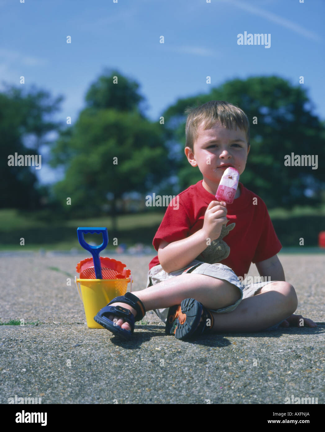 Young Boy Essen ein Eis am Stiel mit Eimer und Spaten Stockfoto