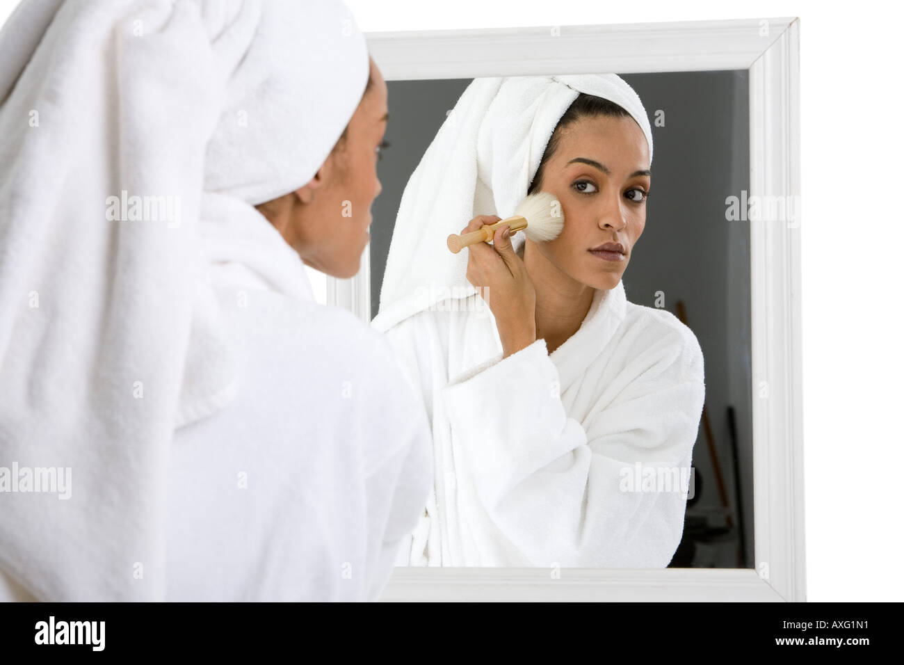 Schöne junge Frau, die auf Make-up vor einem Spiegel tragen ihre Haare in ein Handtuch und weißen Bademantel Stockfoto
