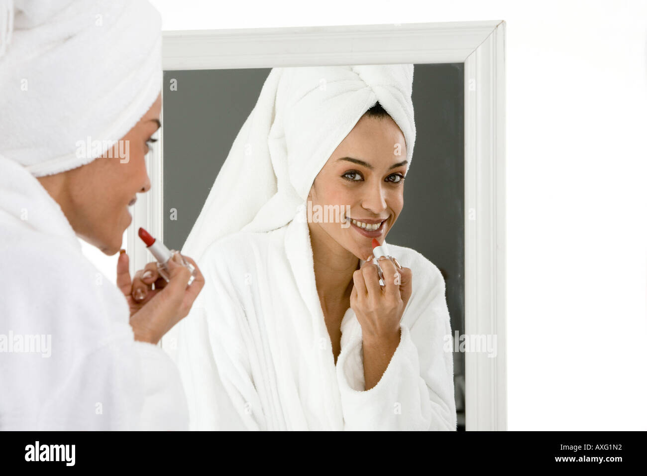 Schöne junge Frau anziehen Lippenstift vor dem Spiegel mit einem Handtuch auf ihr Haar Stockfoto