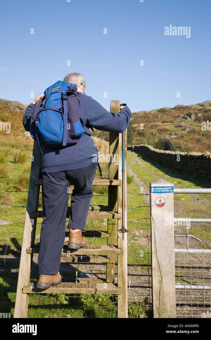 Ältere Dame Wanderer mit Rucksack klettern über Leiter am Anschluss mit offenem Zugang anmelden Snowdonia National Park. Capel Curig Conwy Wales UK Stockfoto