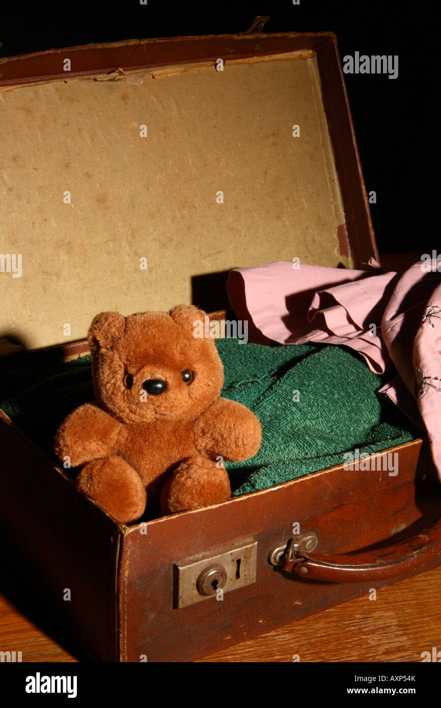 Ein kleiner Teddy Bär sitzt in einem alten offenen Koffer. Stockfoto