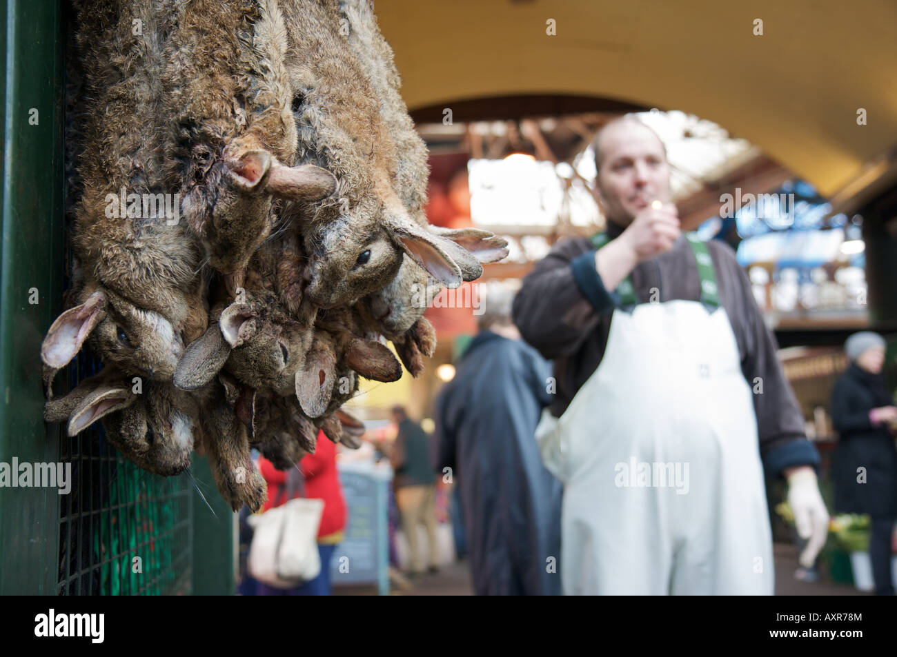 Hasen zum Verkauf in London Borough Market, während ein Fischhändler aufgereiht zündet sich eine Zigarette in den Hintergrund. Stockfoto