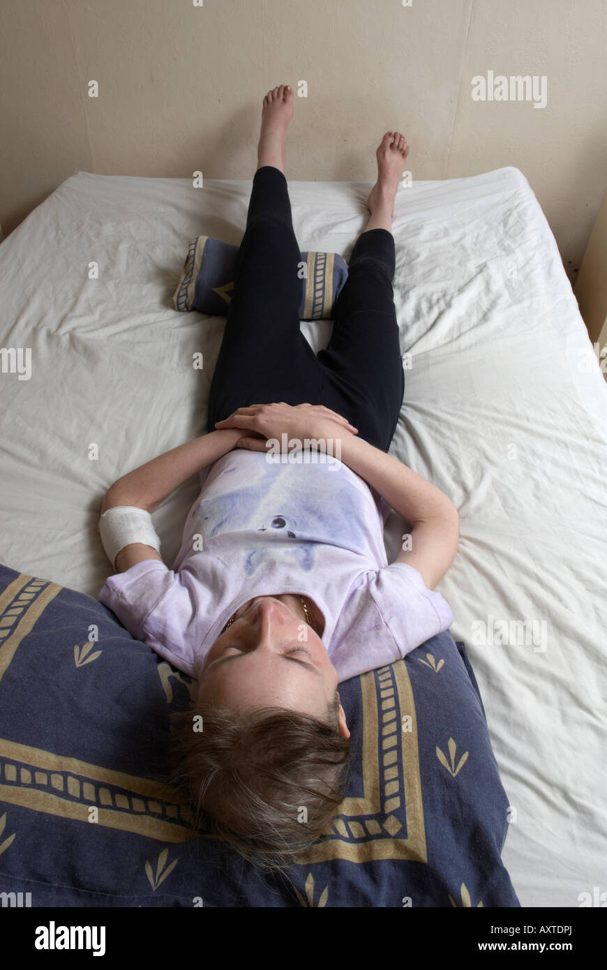 Unwohl Frau Ausübung ihr Bein auf ihrem Bett zwischen Chemotherapie-Behandlungen Stockfoto