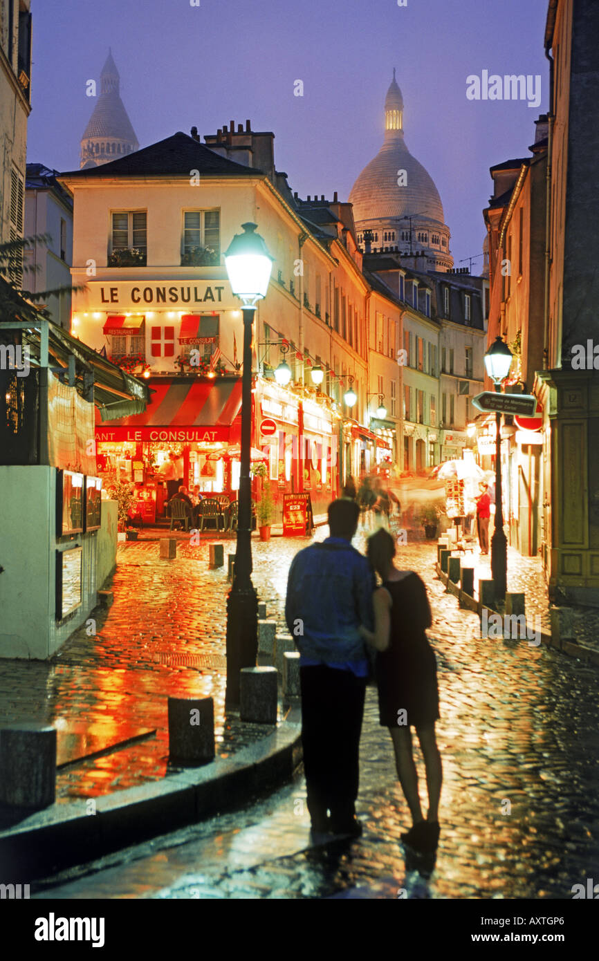 Paar, umarmen, auf nasser Straße mit Kopfsteinpflaster in der Nacht in Montmartre mit Sacre Coeur über Hochhäuser in Paris Stockfoto