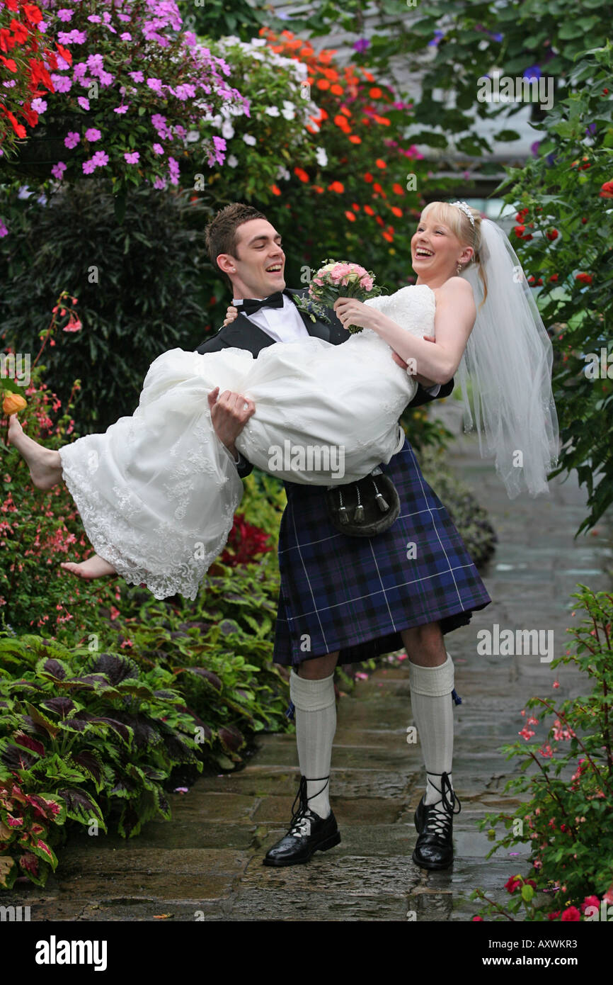 junge schottische Bräutigam seine Braut an ihrem Hochzeitstag tragen Stockfoto