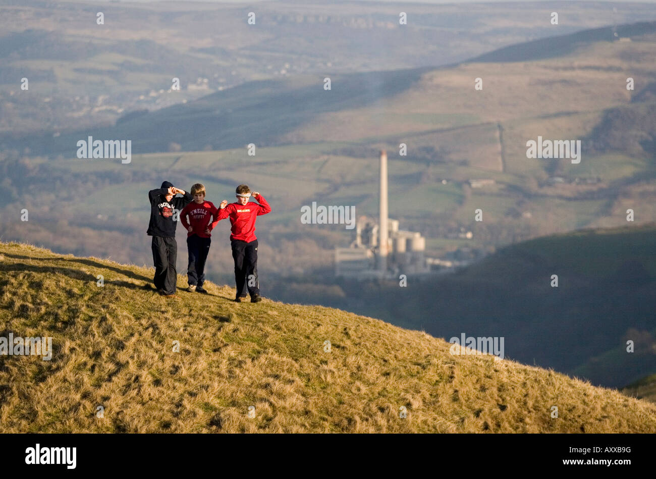 Jungs spielen auf einem Hügel am Mam Tor in der Nähe von Castleton, Peak District National Park, Blue Circle Zementfabrik ist im Hintergrund Stockfoto