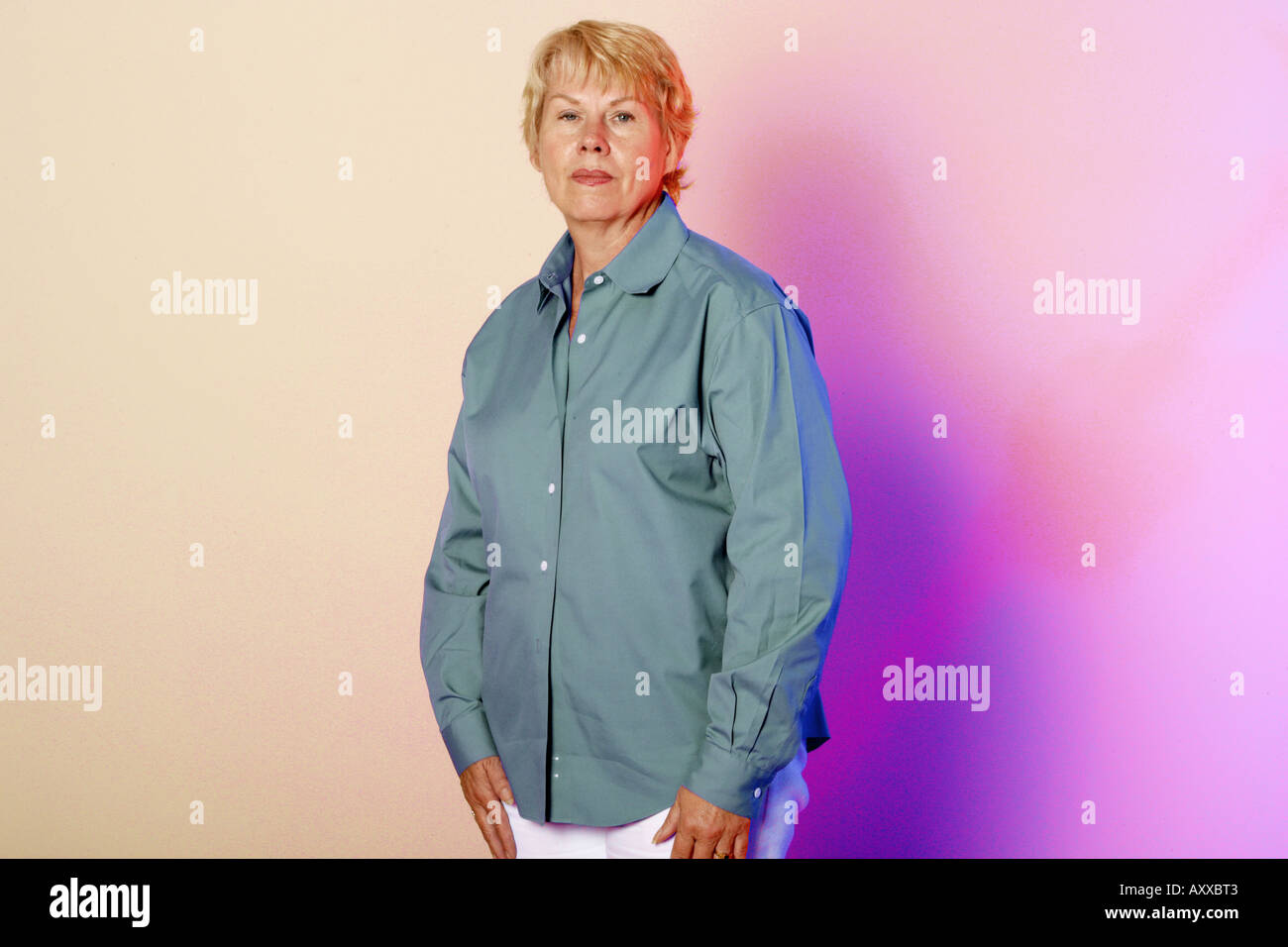 Frau in ihren 60ern, etwas sechzig Jahre alt steht an einer bunt beleuchteten Wand. Stockfoto